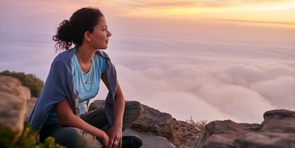 Woman sitting on a mountain overlooking the sunset